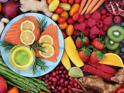 Assorted fruits and vegetables surrounding a plate of raw salmon topped with lemon slices and herbs