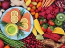 Assorted fruits and vegetables surrounding a plate of raw salmon topped with lemon slices and herbs