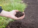Hand holding a handful of dark garden soil over a prepared garden bed