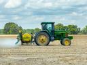 Green tractor spraying a field with yellow tank labeled "REDDICK" attached