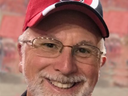 Adult man with glasses and gray beard wearing red cap with block "S" logo, smiling