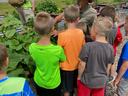 Man wearing hat showing plants to a group of children at raised garden beds