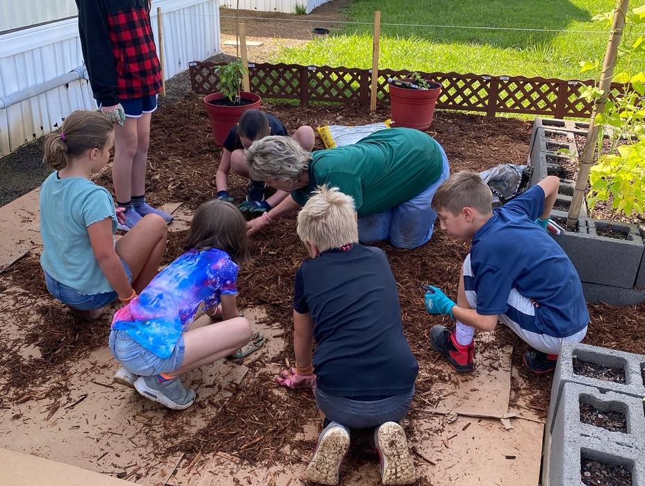 A woman shows children how to spread mulch over cardboard.