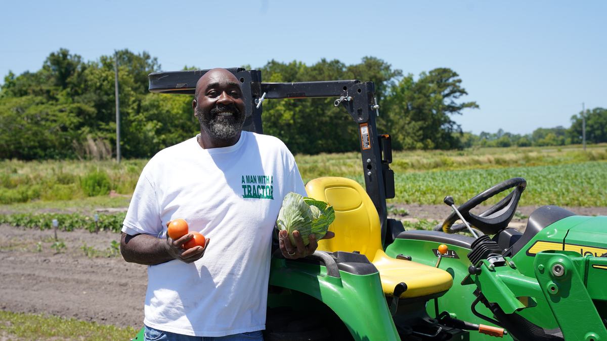 A man holds crops while leaning against a tractor.