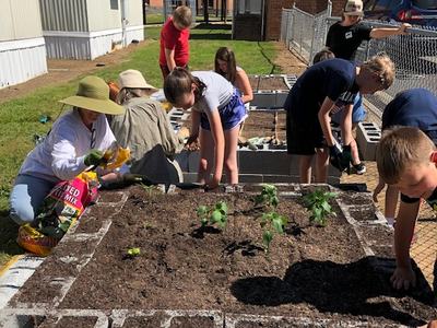7 children and 2 adults working around 2 raised beds.