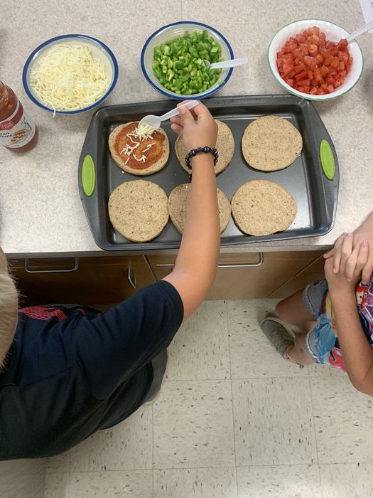 A child makes a personal pizza by spreading cheese over bread and tomato sauce. 