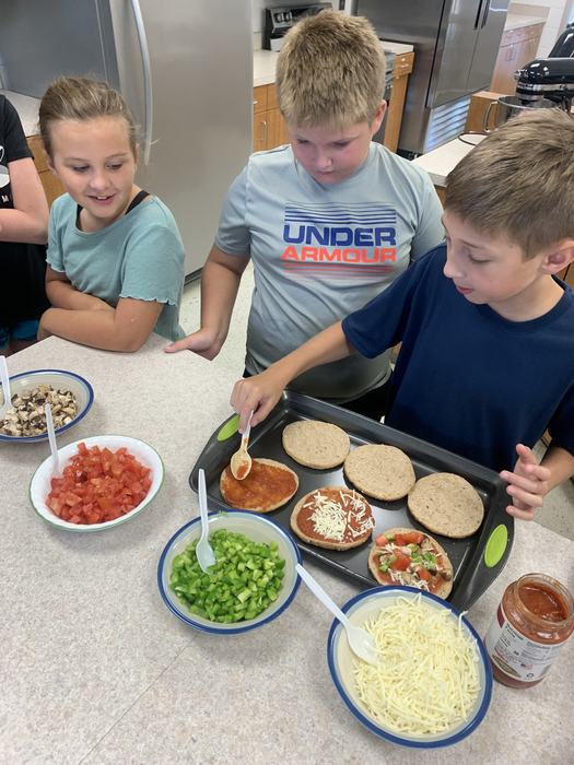 Three children smile over the creation of personal pizzas. 