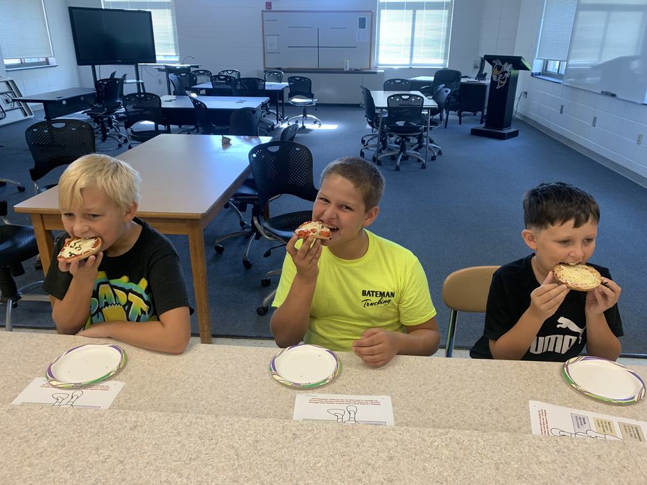 Children sit at a table eating pizzas they made. 