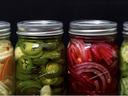 Four glass jars with pickled vegetables (jalapeños, red onions, cucumbers, slaw)