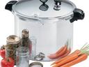 Stainless steel pressure cooker with gauge, canning jars and lids, fresh carrots and a tomato