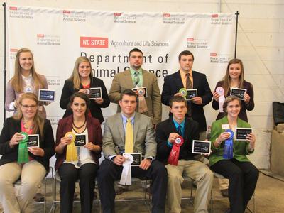 Teenagers display their awards while standing in from of the Department of Animal Science Banner.