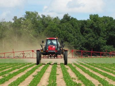 A tractor sprays pesticides over a field.