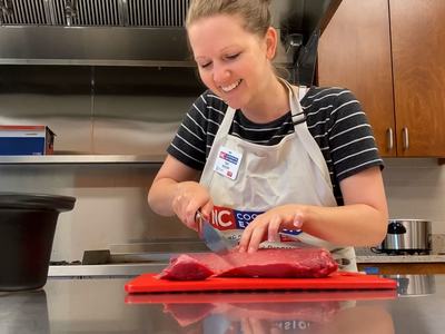 Person in apron slicing raw beef on a red cutting board in a kitchen.