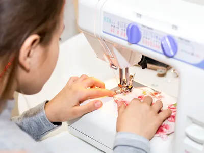 Hands guiding floral fabric through the needle of a sewing machine