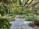 Gravel garden path framed by wooden pergola, circular planting beds and bench