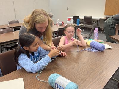 A woman shows two children how to crochet.