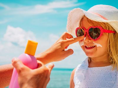 putting sunscreen on child wearing sunglasses and hat
