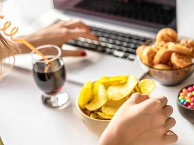 Girl works at a computer and eats unhealthy food. 