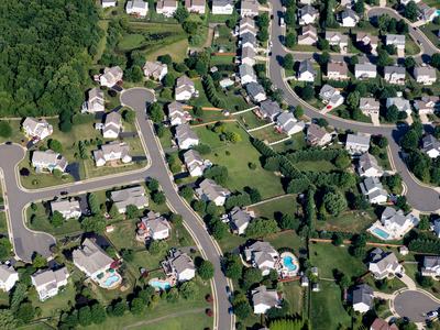 Suburban neighborhood seen from above with houses, curved streets, yards, and pools