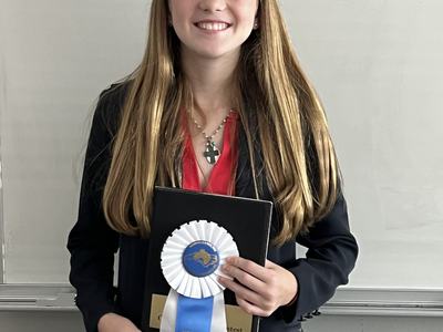 Young person holding a plaque and blue ribbon labeled "North Carolina State 4‑H Horse Program"