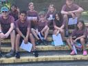 Children in matching maroon shirts sitting on outdoor steps holding papers