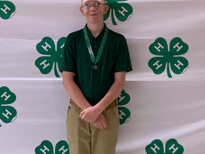Youth standing with medal in front of 4‑H clover logo backdrop