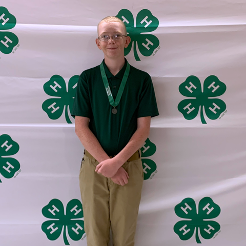 Youth standing with medal in front of 4‑H clover logo backdrop