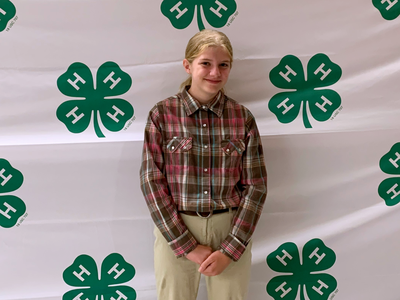 Young person standing in front of white backdrop patterned with green 4-H clover logos