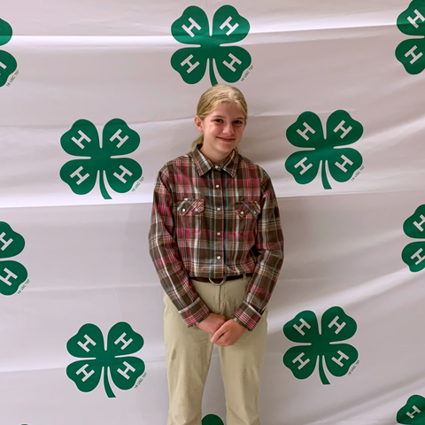 Young person standing in front of white backdrop patterned with green 4-H clover logos