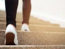 Lower legs and white sneakers ascending carpeted stairs
