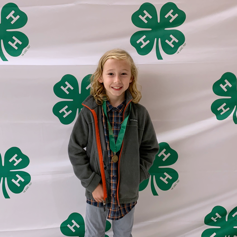 Young child wearing a medal standing in front of repeating 4‑H clover logos