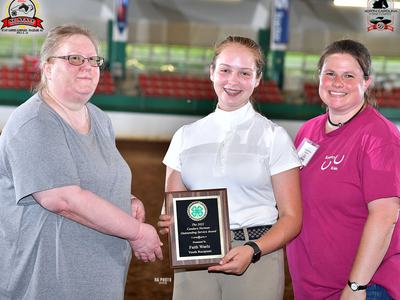 Teen holding plaque "Candace Norman Outstanding Service Award – Faith Waelz" flanked by two adults