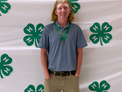 Teen wearing a medal stands in front of a 4-H clover backdrop