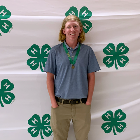 Teen wearing a medal stands in front of a 4-H clover backdrop