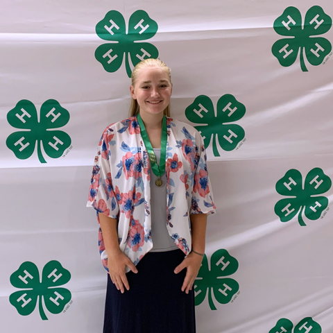 Person with medal standing in front of repeating green 4‑H clover logo backdrop