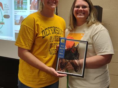 Two people holding framed horse art with blue ribbon reading "West District 4‑H Horse"