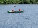 Two green canoes on a lake with people in life jackets paddling near a treeline