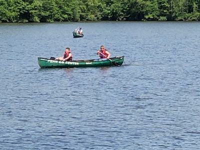 Two green canoes on a lake with people in life jackets paddling near a treeline
