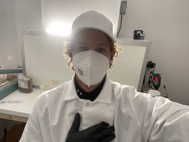 A man in a clean white jacket and hat wearing a surgical mask.