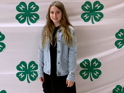Girl standing in front of a backdrop with repeating green 4‑H clover logos