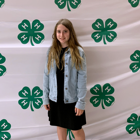 Girl standing in front of a backdrop with repeating green 4‑H clover logos