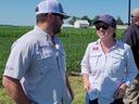 Two people wearing NC State shirts and caps talking in a crop field