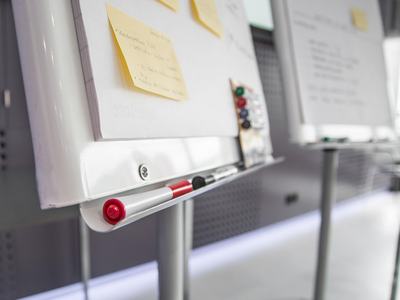 Whiteboard easel edge with red and black markers and yellow sticky notes