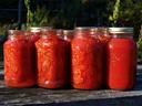 Seven mason jars filled with canned tomatoes arranged on a wooden surface
