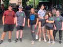 Seven teenagers standing under a pavilion at an outdoor market, posing for a photo