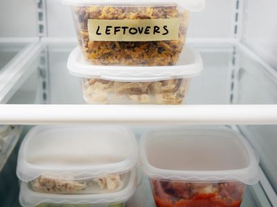 Plastic food containers stacked in refrigerator, top one labeled "LEFTOVERS"