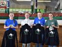 Four youth holding jackets labeled "NC State 4-H Horse Program" in indoor arena