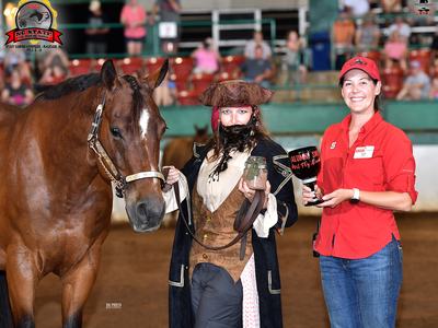 Brown horse led by person in pirate costume holding jar; woman in red holds trophy reading ALUMNI