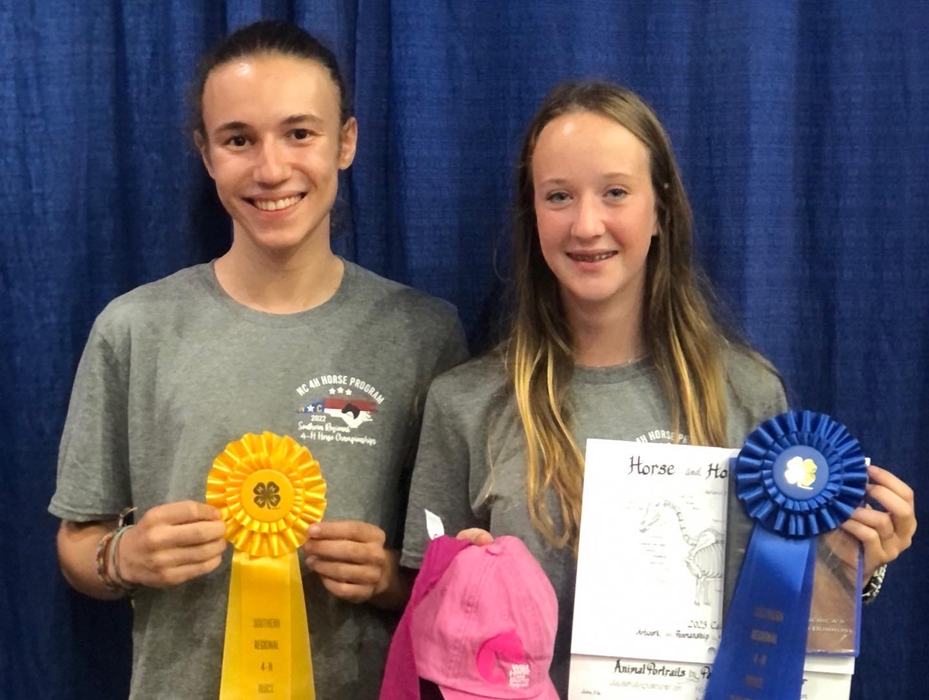Two youths holding yellow and blue ribbons and horse certificates against a blue curtain