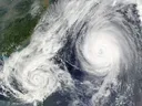 Two large tropical cyclones with clear eyes over the ocean, one closer to a nearby coastline